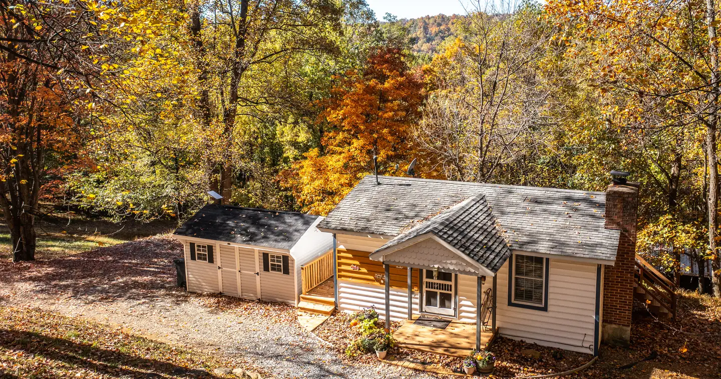 A white cottage among fall trees in peak color, with a mountain ridge behind