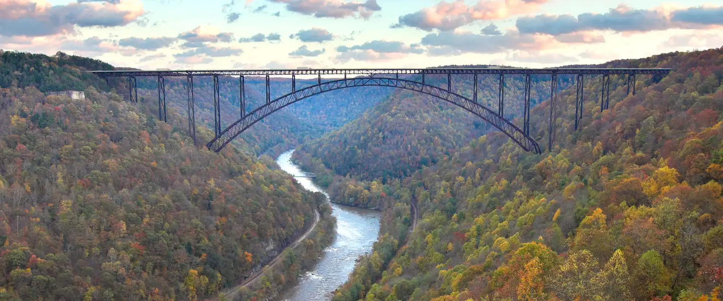 The New River Gorge Bridge arching over the river, with fall color on both sides of the gorge