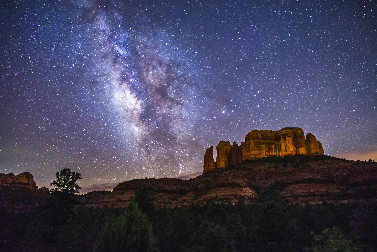The Milky Way rising over Cathedral Rock, its red cliffs lit warm against a starry sky